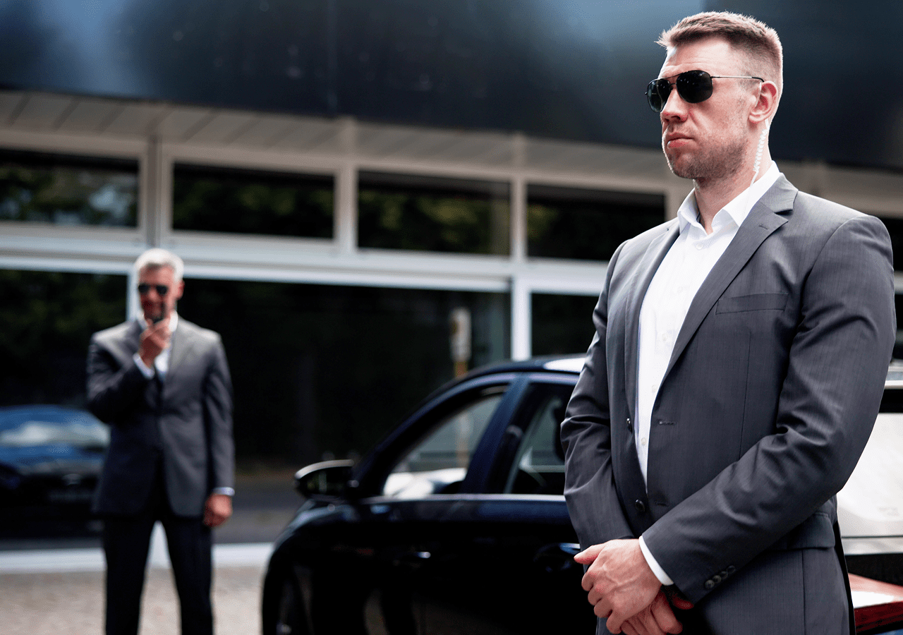 Two men in suits near black car.